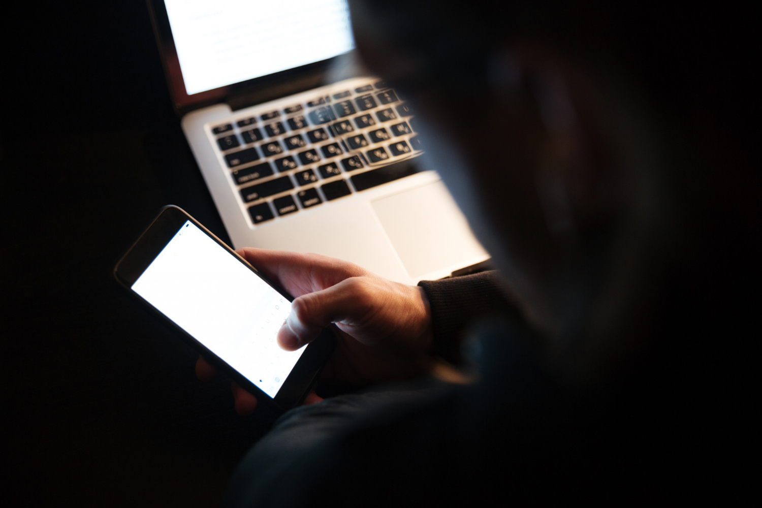 alt="Persona usando el celular junto a una notebook por la noche, alerta por estafa de streaming gratis"